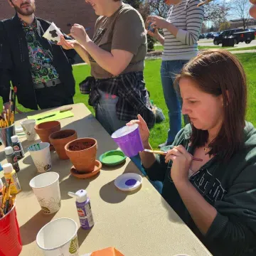 four students paint pots outside