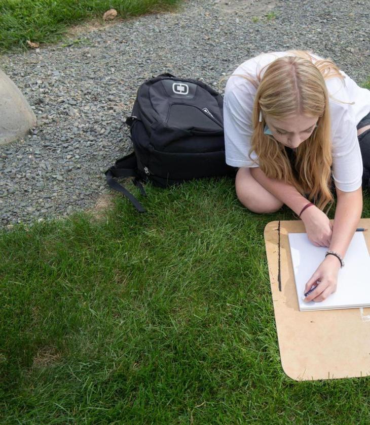 Student draws using a clipboard in the grass for an outdoor art class